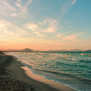An image of a beach overlook. The sun is setting over an ocean with mountains in the background.